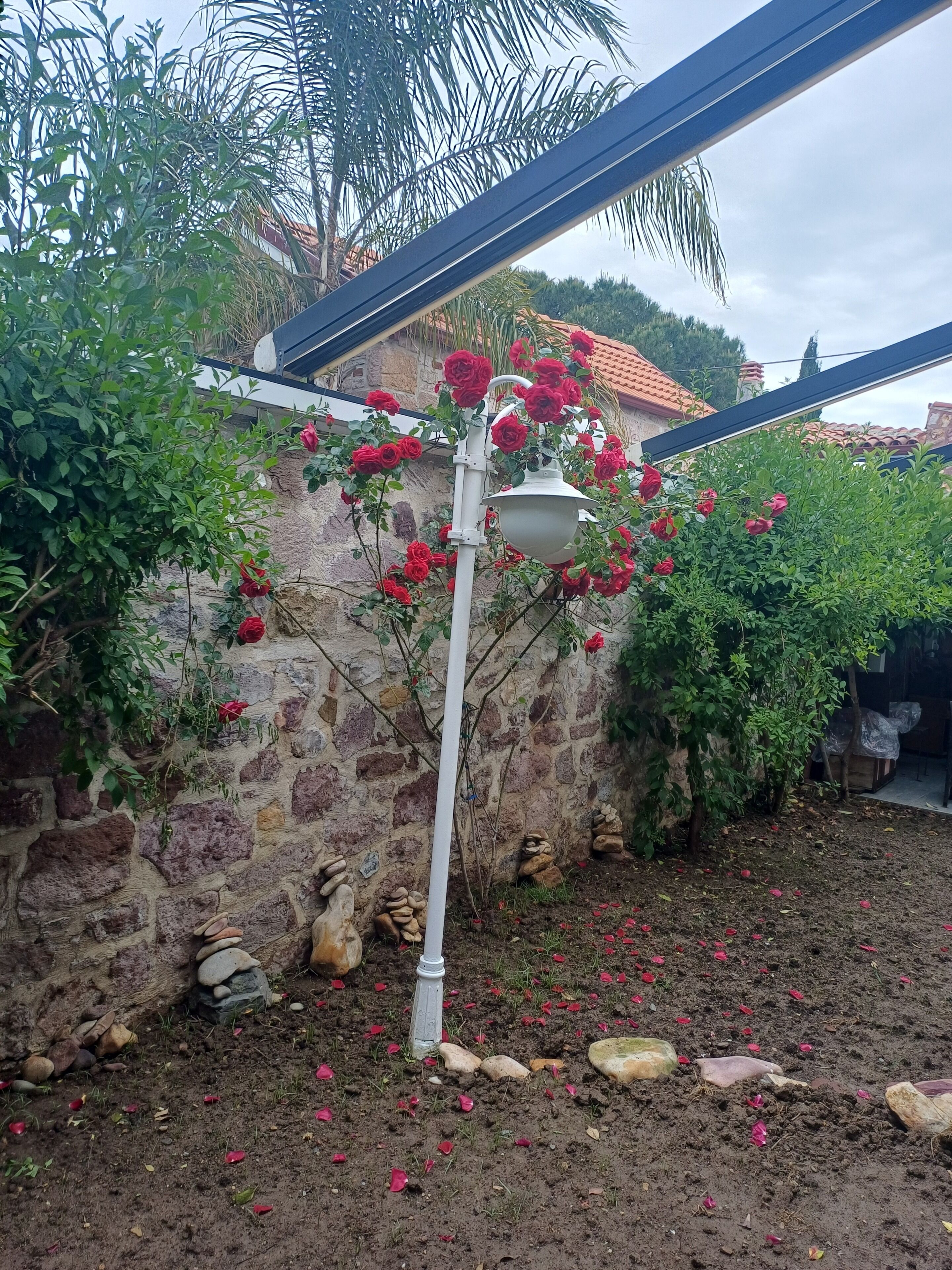 Een stenen muur met een witte lantaarnpaal en rode bloemen.