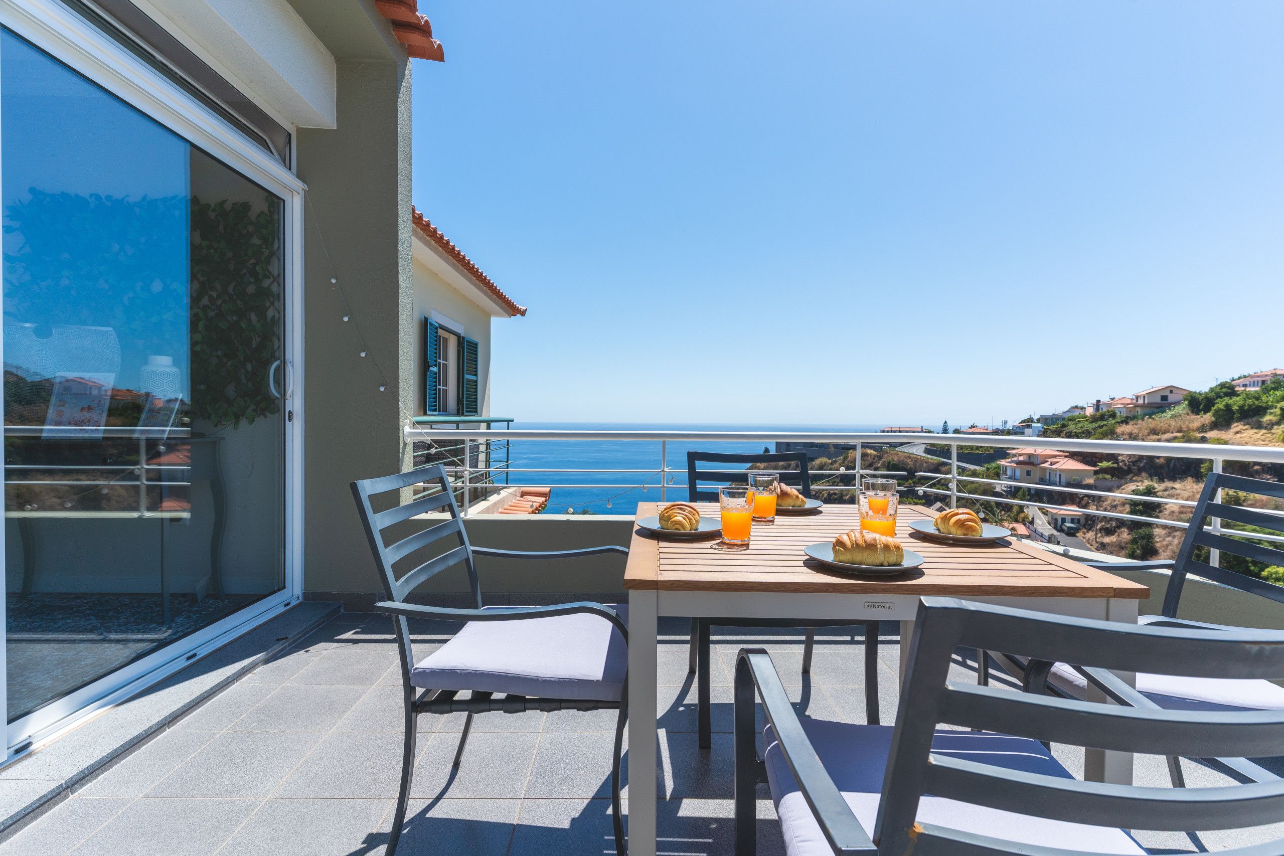 A balcony with a table set for breakfast, overlooking a coastal view.