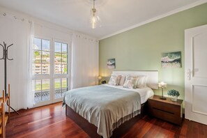 Ein Schlafzimmer mit einem Bett, Nachttischen, einer Lampe und Blick auf Gebäude durch das Fenster.