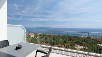 A balcony with a table and chairs, overlooking a coastal view with a railing and vegetation.