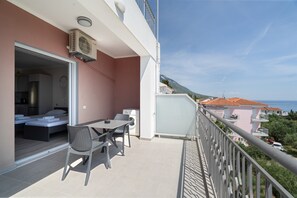 A balcony with a table and chairs, a washing machine, and a bed in the adjacent room. - Intimate Sea View Studio for Two in Kefalonia (Vlachata)