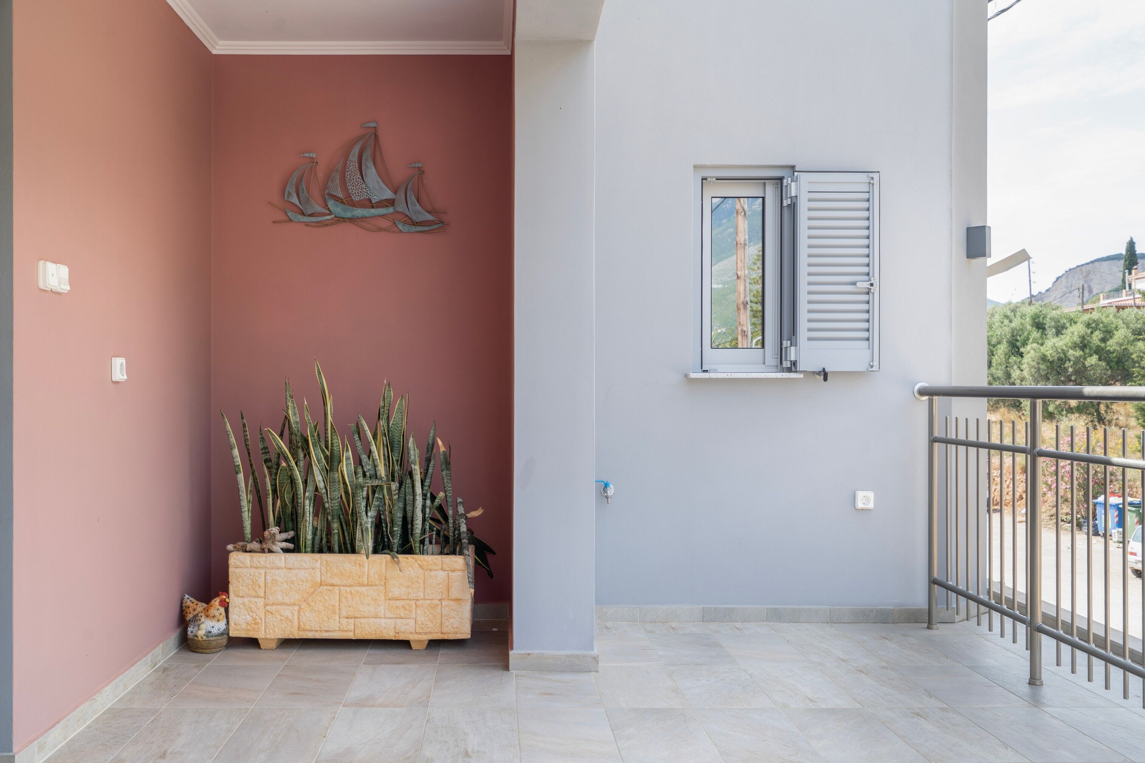 Un balcon avec une balustrade en métal, un pot de fleurs, une fenêtre avec des volets et un élément décoratif fixé au mur.