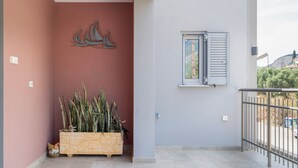 Un balcone con ringhiera in metallo, una pianta in vaso, una finestra con persiane e un elemento decorativo a parete.