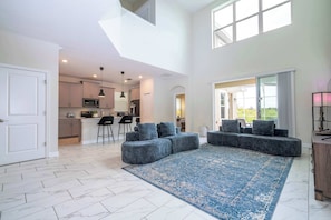 A spacious living area with a large blue rug, grey sectional sofa, and a kitchen in the background. - Spacious 5BR at ChampionsGate - Hot Tub! (Kissimmee)