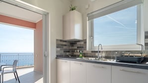 A modern kitchen with a large window, a balcony with a view, and a dining area with chairs.