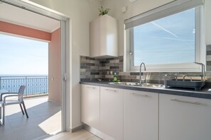 A modern kitchen with a large window, a balcony with a view, and a dining area with chairs. - Seaside Retreat with Stunning Sea Views in Kefalonia (Vlachata)