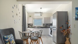 A modern kitchen with a dining area, a grey sofa, and a wall clock.