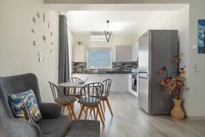 A modern kitchen with a dining area, a grey sofa, and a wall clock. - Seaside Retreat with Stunning Sea Views in Kefalonia (Vlachata)