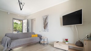 A modern living room with a sofa, a small side table, a TV mounted on the wall, and a window with a view.