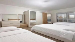 Habitación de hotel con dos camas, un armario, un espejo y puerta corrediza a un balcón.
