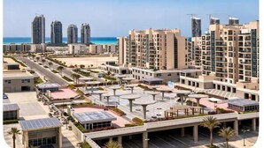 Complejo residencial de edificios altos con múltiples balcones, un patio central con asientos y vista a la playa.