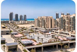 A high-rise residential building complex with multiple balconies, a central courtyard with seating, and a beach view.