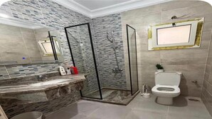 Un baño con cabina de ducha de vidrio, tocador de mármol y un inodoro.