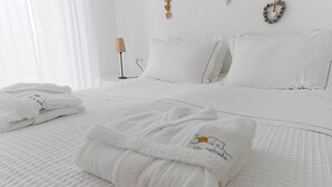 A neatly made bed with white bedding, a folded towel with a logo, and a bedside lamp. - On The Rocks - The Retreat - Serviced Studio (Ios)