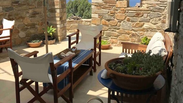 A stone-walled outdoor seating area with a view of the sea, a table with chairs, and potted plants. - On The Rocks - The Retreat - Serviced Studio (Ios)