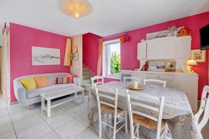 Ein Zimmer mit einem weißen Sofa, einem Esstisch mit Stühlen, einer Küchenzeile und einem Fenster mit Vorhängen.