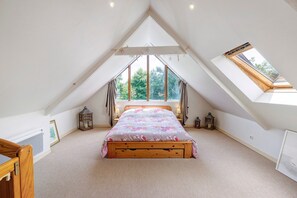 Ein Schlafzimmer mit schrägen Wänden, einem Bett, zwei Fenstern und einem Oberlicht.