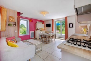Ein helles Wohnzimmer mit einer Couch, einem Esstisch und einer Küchenzeile mit Gasherd.