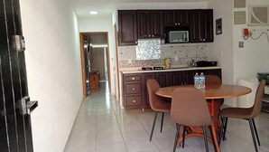 Una cocina con armarios oscuros, salpicadero de azulejos, un microondas y un comedor con una mesa redonda y cuatro sillas.