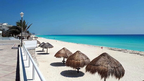 Una playa con sombrillas de paja, una barandilla blanca y un cielo azul despejado.