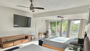 Un dormitorio con una cama grande, un escritorio, una silla, un televisor y un ventilador de techo.