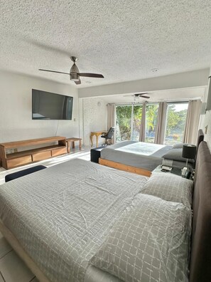 Ein Schlafzimmer mit einem großen Bett, einem Schreibtisch, einem Sessel, einem Fernseher und einem Deckenventilator.