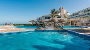 Una piscina con cubierta de madera, palmeras y un edificio al fondo.