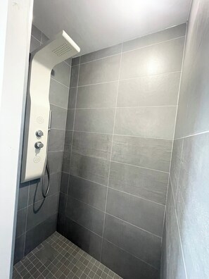 A shower area with a wall-mounted showerhead, a handheld showerhead, and a control knob.