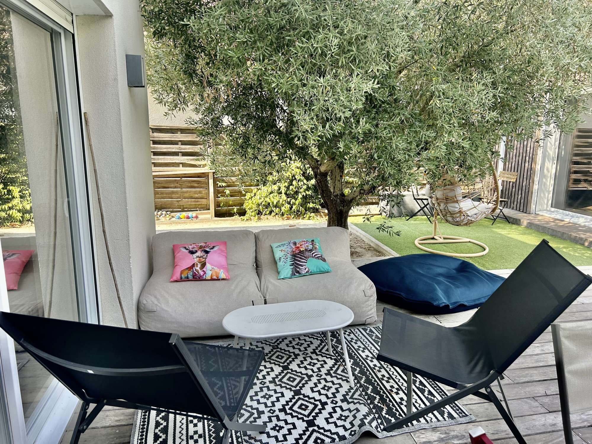 Eine Terrasse mit einer Sitzecke, zwei Stühlen, einem kleinen Tisch und einem gemusterten Teppich.