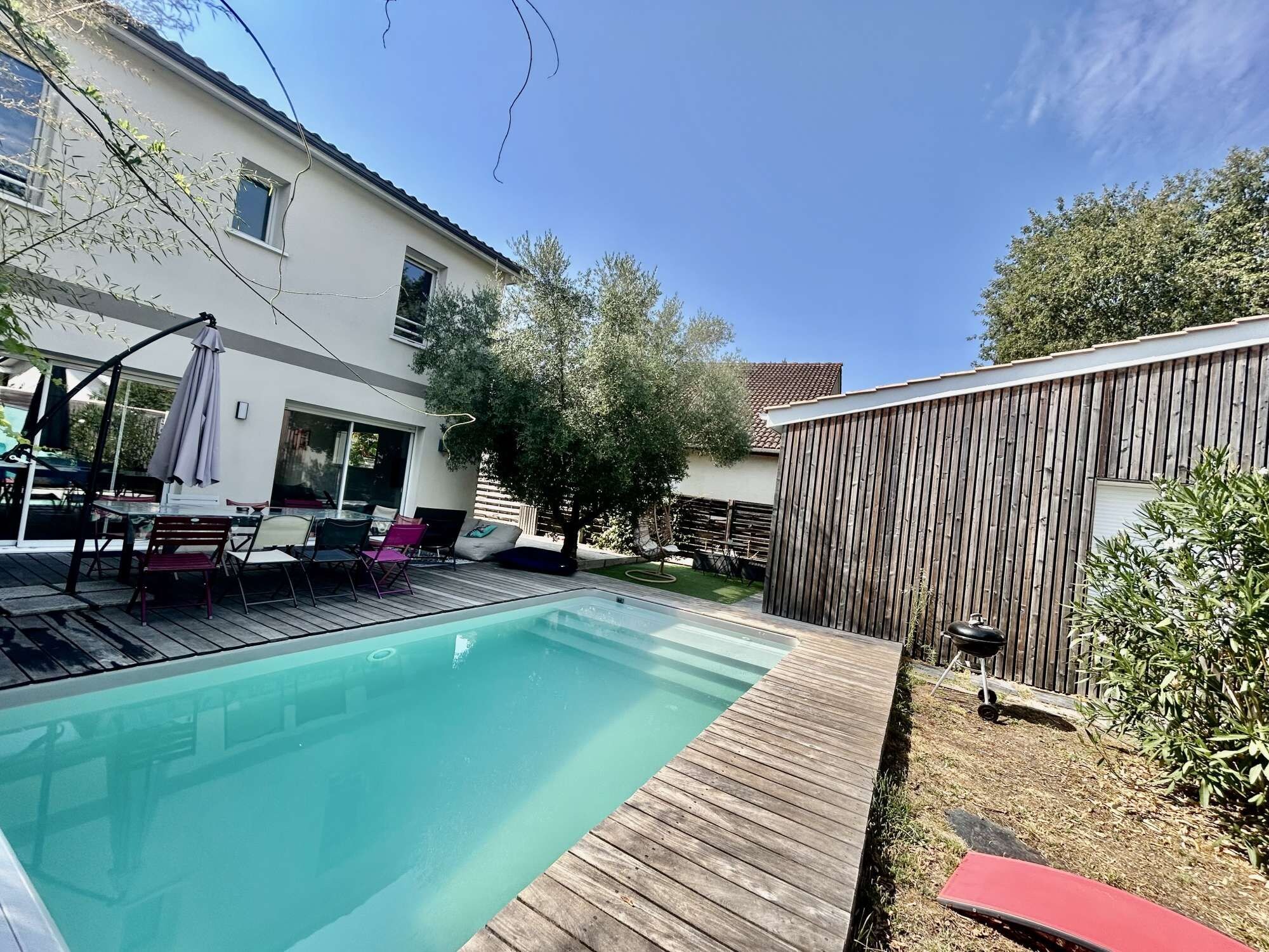 Ein Garten mit Swimmingpool, Holzterrasse, Grill und umzäunter Bereich.
