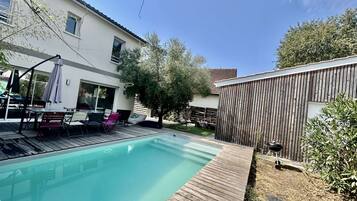 Ein Garten mit Swimmingpool, Holzterrasse, Grill und umzäunter Bereich.