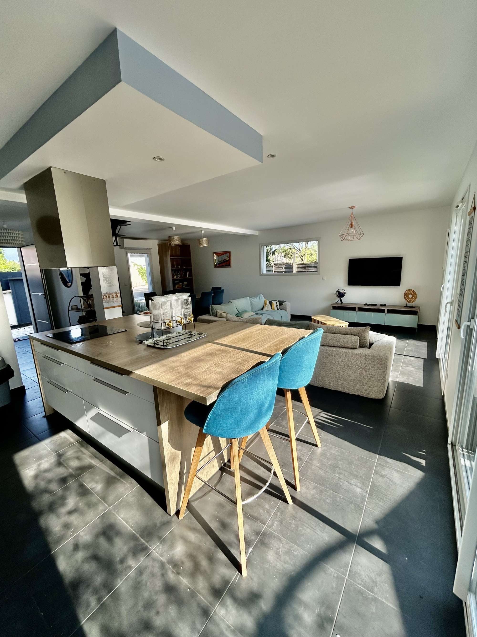 Una cucina moderna con isola centrale, sedie blu, un divano e una TV.