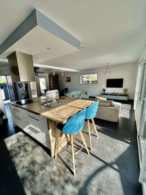 Een moderne keuken met een centraal eiland, blauwe stoelen, een bank en een televisie.