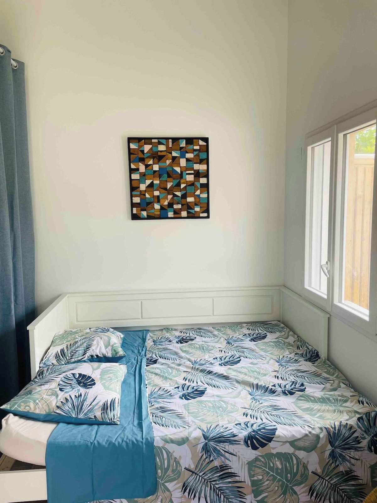 A bedroom with a bed, a window, and a wall-mounted artwork.