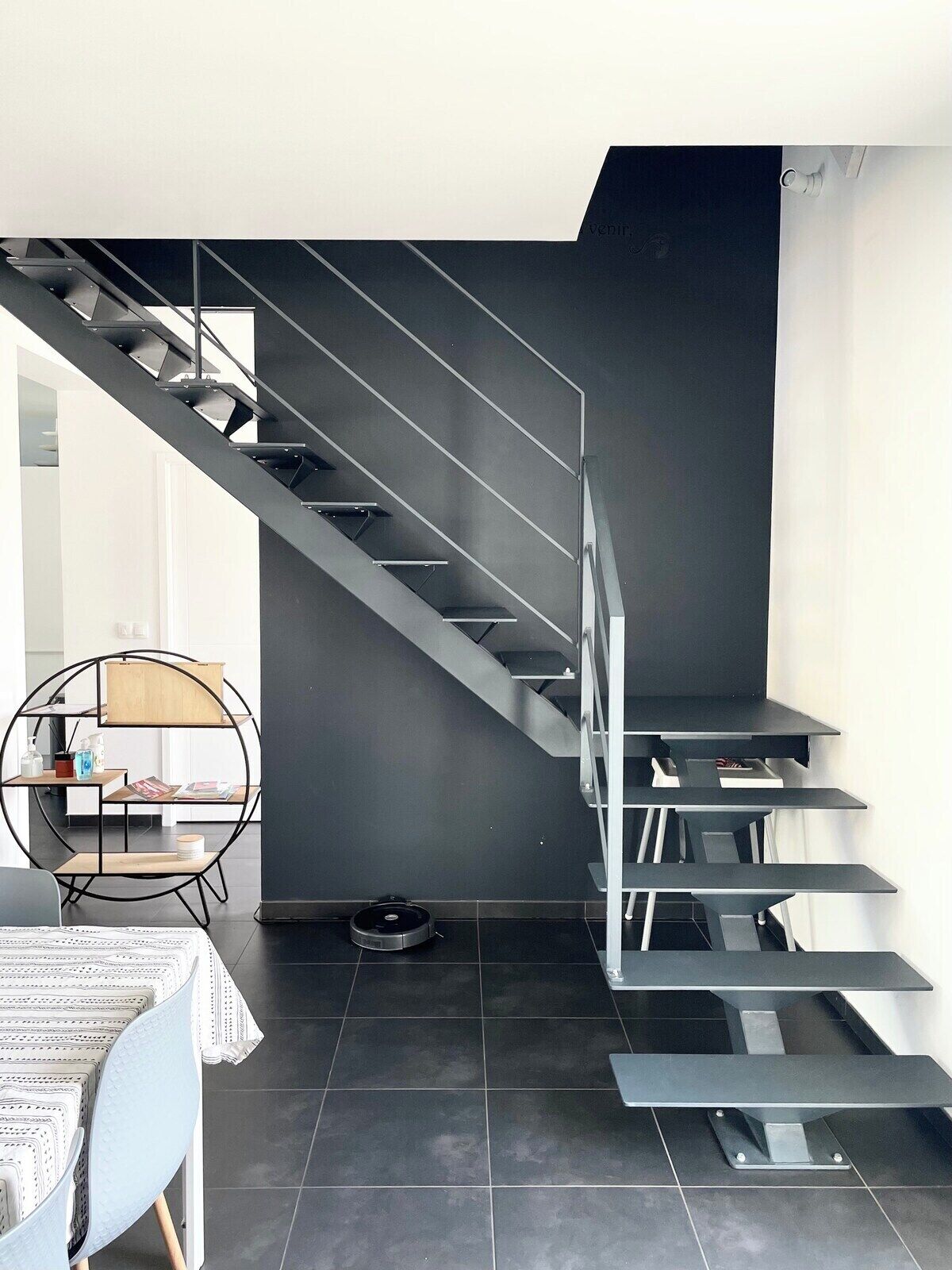 Ein modernes Interieur mit einer Treppe, einem runden Tisch mit einem Stuhl und einem kleinen Saugroboter.