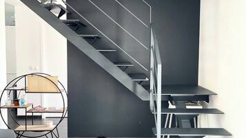 Ein modernes Interieur mit einer Treppe, einem runden Tisch mit einem Stuhl und einem kleinen Saugroboter.