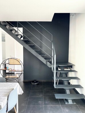 Ein modernes Interieur mit einer Treppe, einem runden Tisch mit einem Stuhl und einem kleinen Saugroboter.