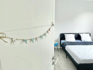 A bedroom with a bed, a wall-mounted string of triangular flags, and a small blue stool.