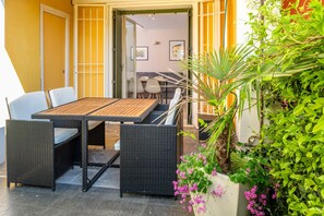Una zona patio con tavolo e sedie, un divano in vimini e una pianta in vaso fiorita.