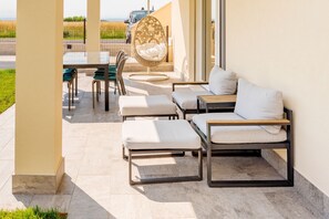 Een terras met buitenmeubilair, waaronder een bank, stoelen en een hangstoel.