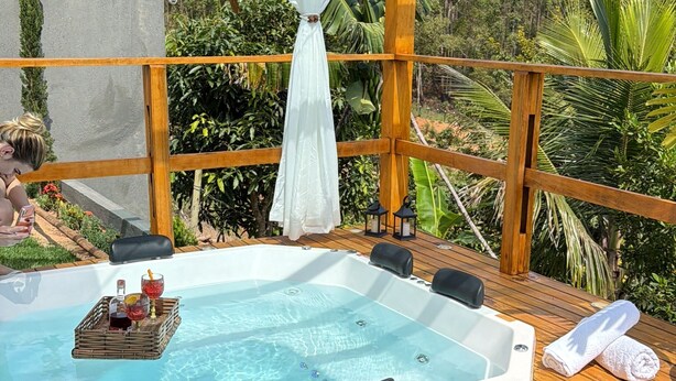 Una terraza de madera con un jacuzzi, una cortina blanca y vistas a un bosque.