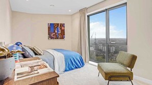 Un dormitorio moderno con un ventanal grande, una cama, una silla y una mesa con revistas.