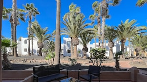A patio with outdoor seating, palm trees, and white buildings in the background.