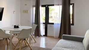 A room with a round dining table, white chairs, a ceiling fan, and a sofa.