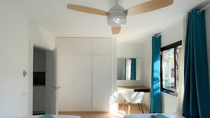 A room with two beds, a desk, a ceiling fan, a wardrobe, and a window with curtains.