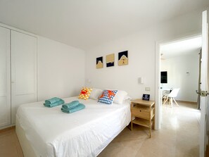 Une chambre d’hôtel avec un lit, un bureau et une chaise. On trouve des serviettes sur le lit, une lampe de bureau et un téléviseur fixé au mur.