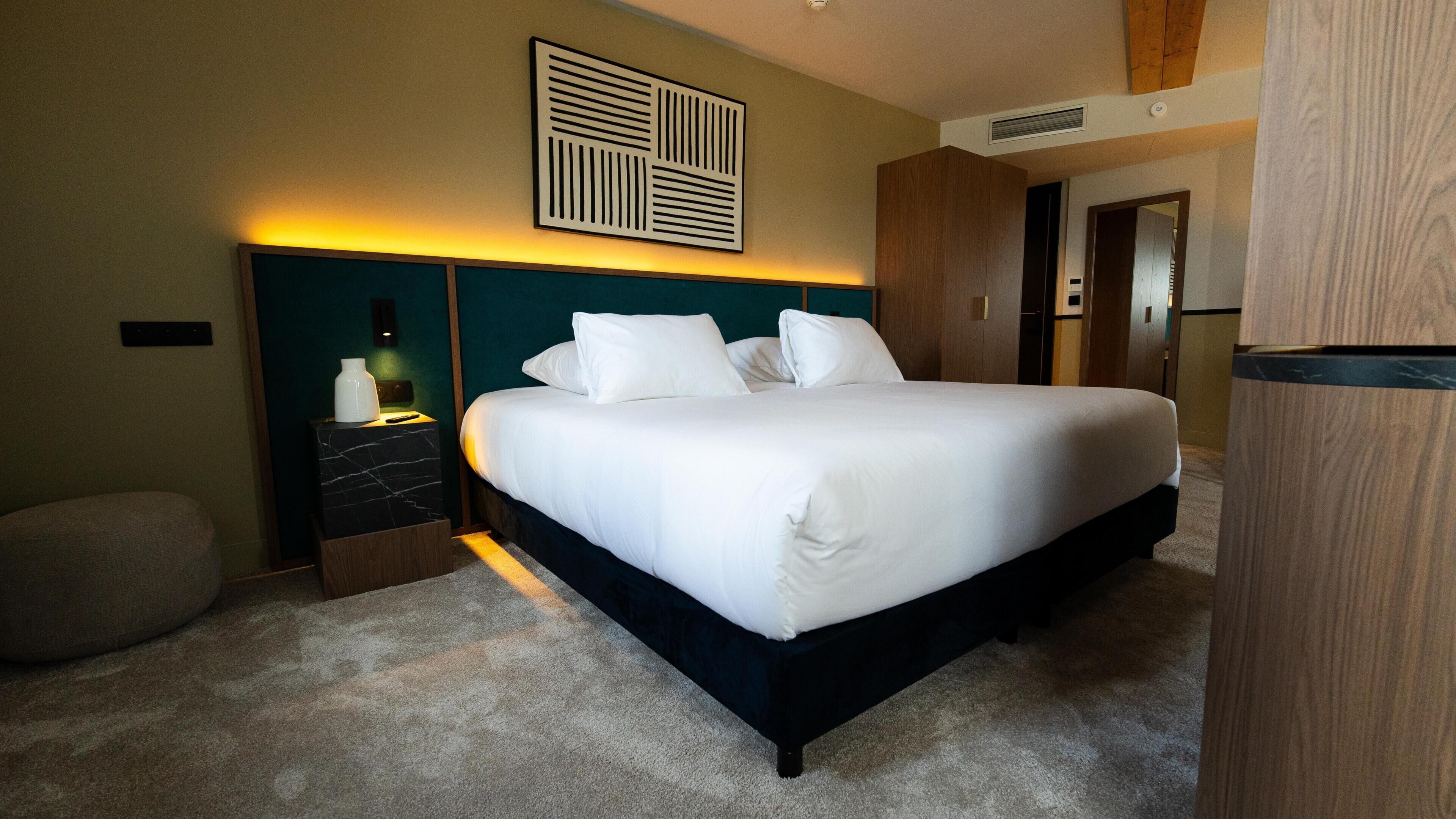 Une chambre à coucher bien rangée, avec un lit, des tables de chevet, une lampe fixée au mur et une porte.