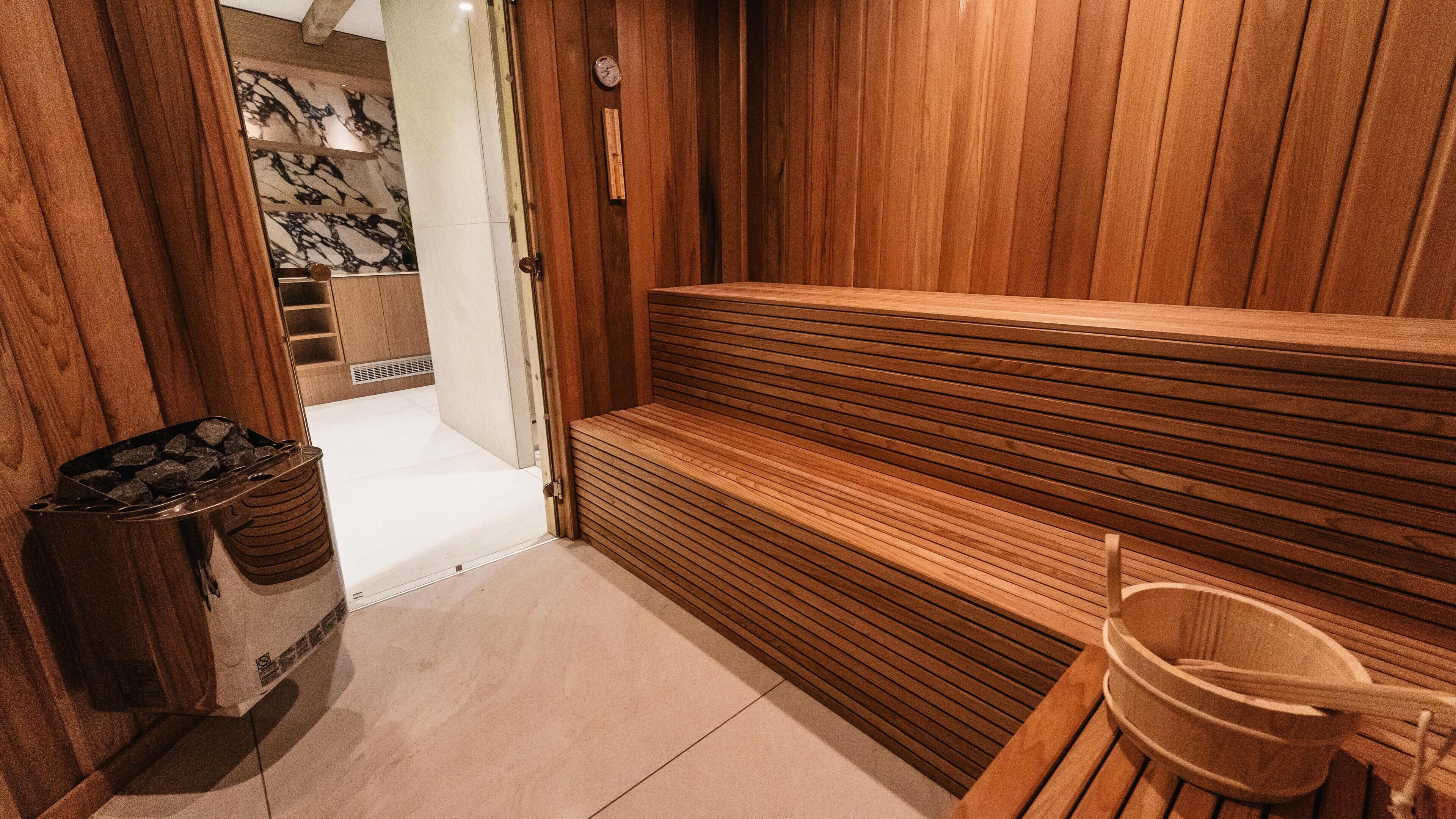 Una sauna con bancos de madera, un cubo de madera y un contenedor de basura.