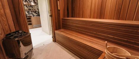 Una sauna con bancos de madera, un cubo de madera y un contenedor de basura.