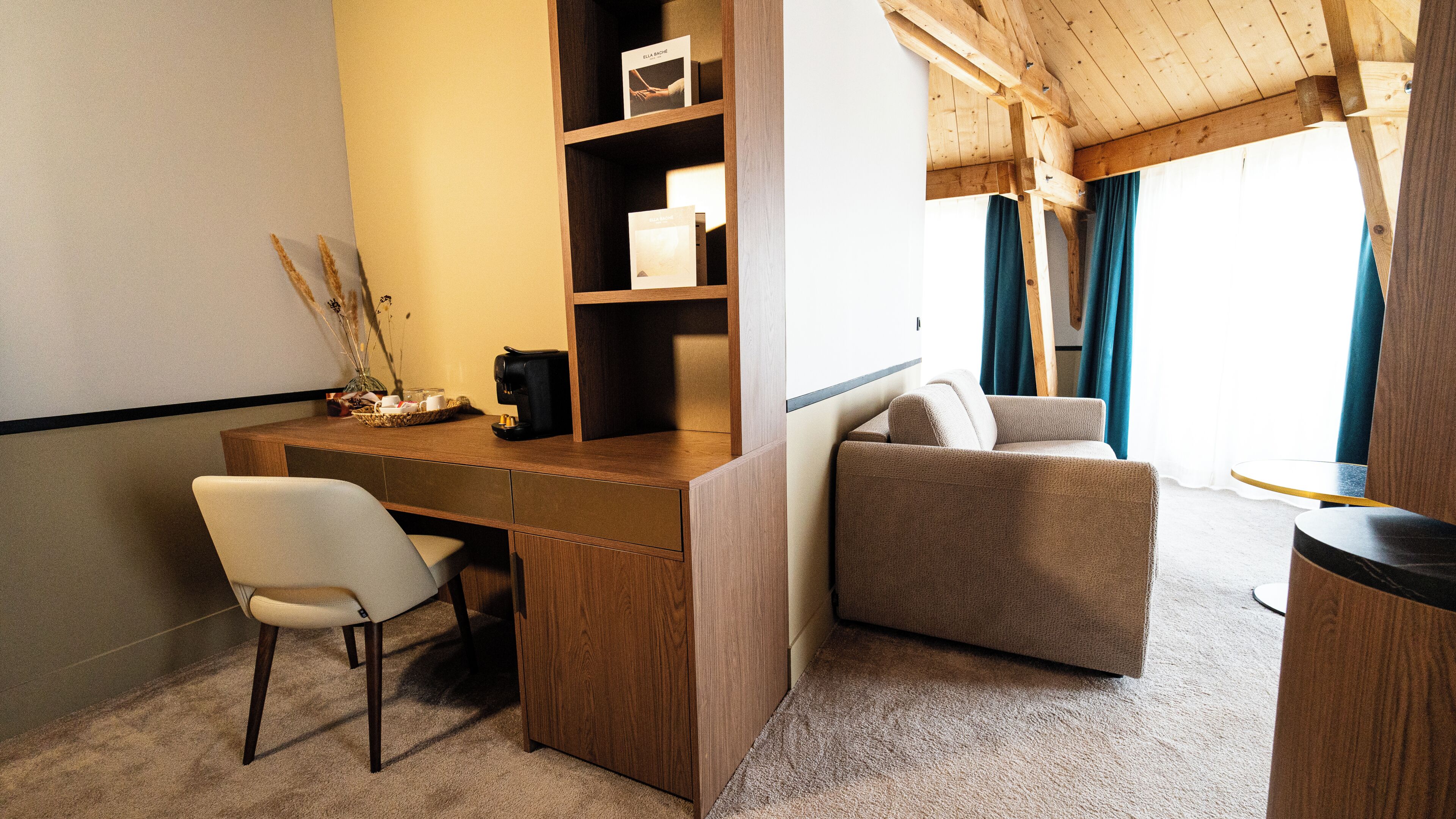 A room with a wooden desk, a chair, a sofa, a coffee maker, and a bookshelf.